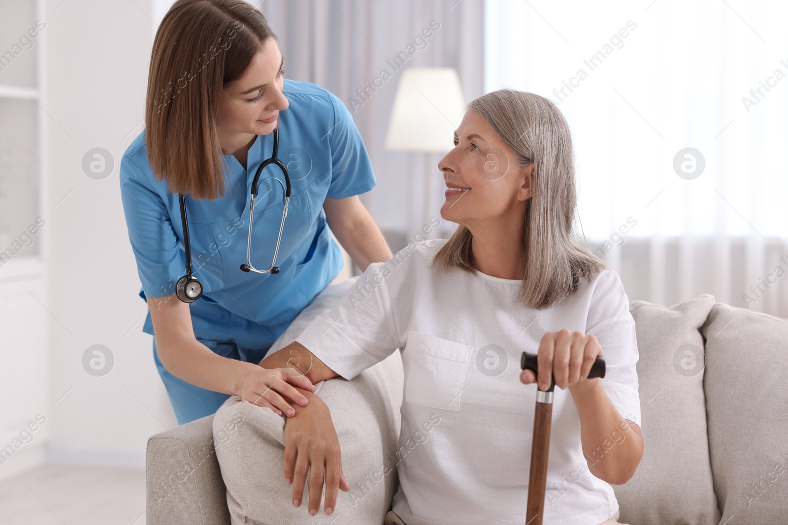 Photo of Young healthcare worker supporting senior patient indoors