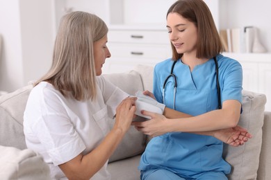 Photo of Young healthcare worker measuring patient's blood pressure indoors