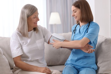 Smiling healthcare worker measuring patient's blood pressure indoors