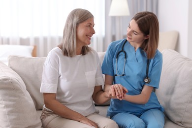 Photo of Young healthcare worker supporting senior patient indoors