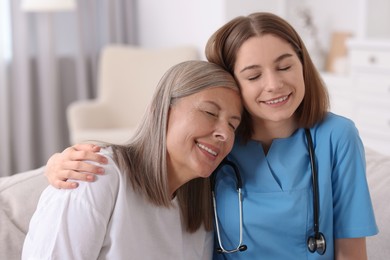 Photo of Smiling healthcare worker supporting senior patient indoors