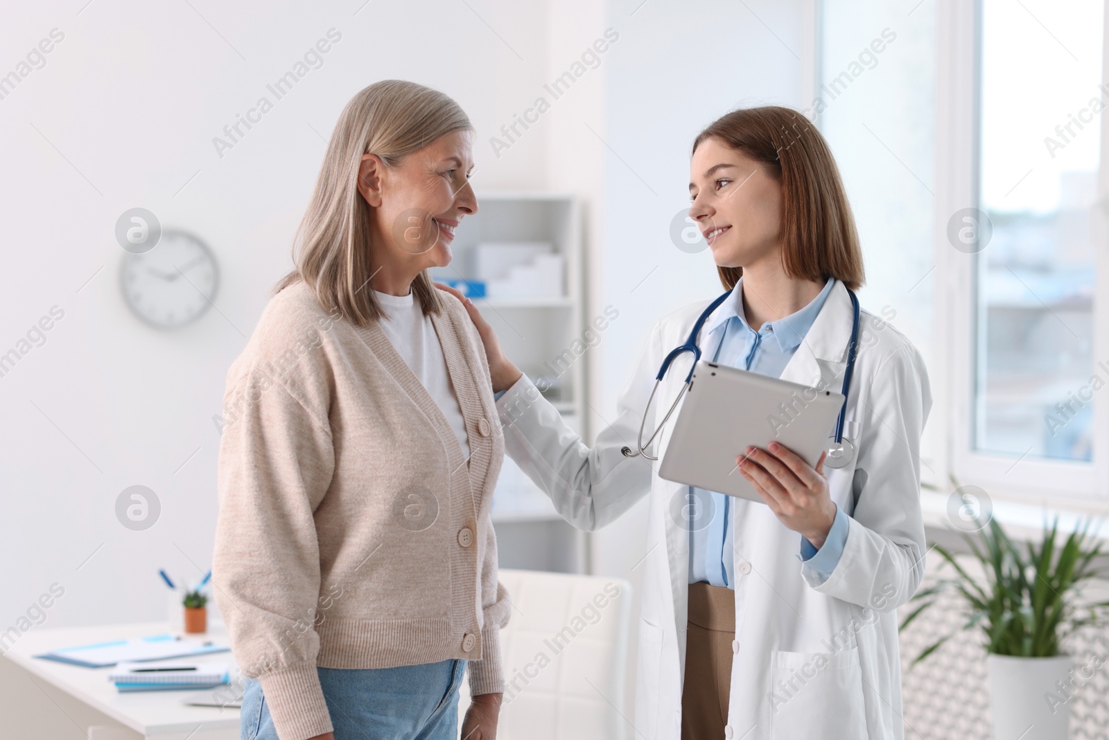 Photo of Smiling healthcare worker with tablet supporting senior patient in hospital