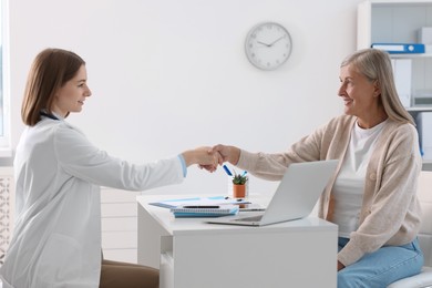 Smiling healthcare worker shaking hands with senior patient in hospital