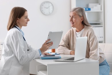 Photo of Smiling healthcare worker with tablet consulting senior patient in hospital