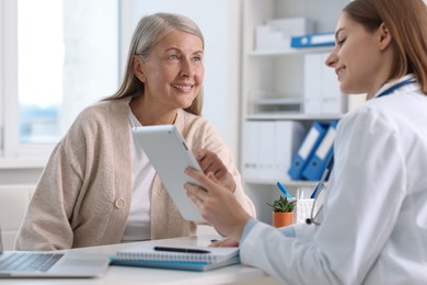 Photo of Smiling healthcare worker with tablet consulting senior patient in hospital