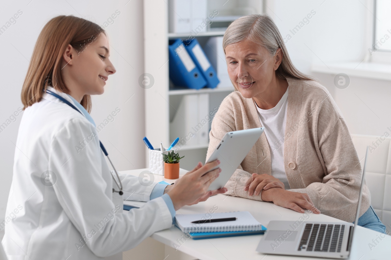 Photo of Smiling healthcare worker and senior patient checking analysis results on tablet in hospital