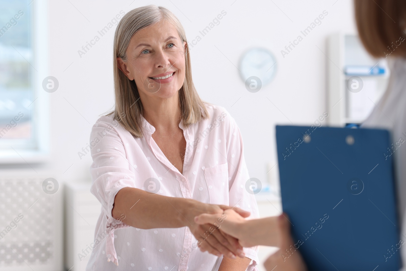 Photo of Smiling patient shaking hands with healthcare worker in hospital, closeup