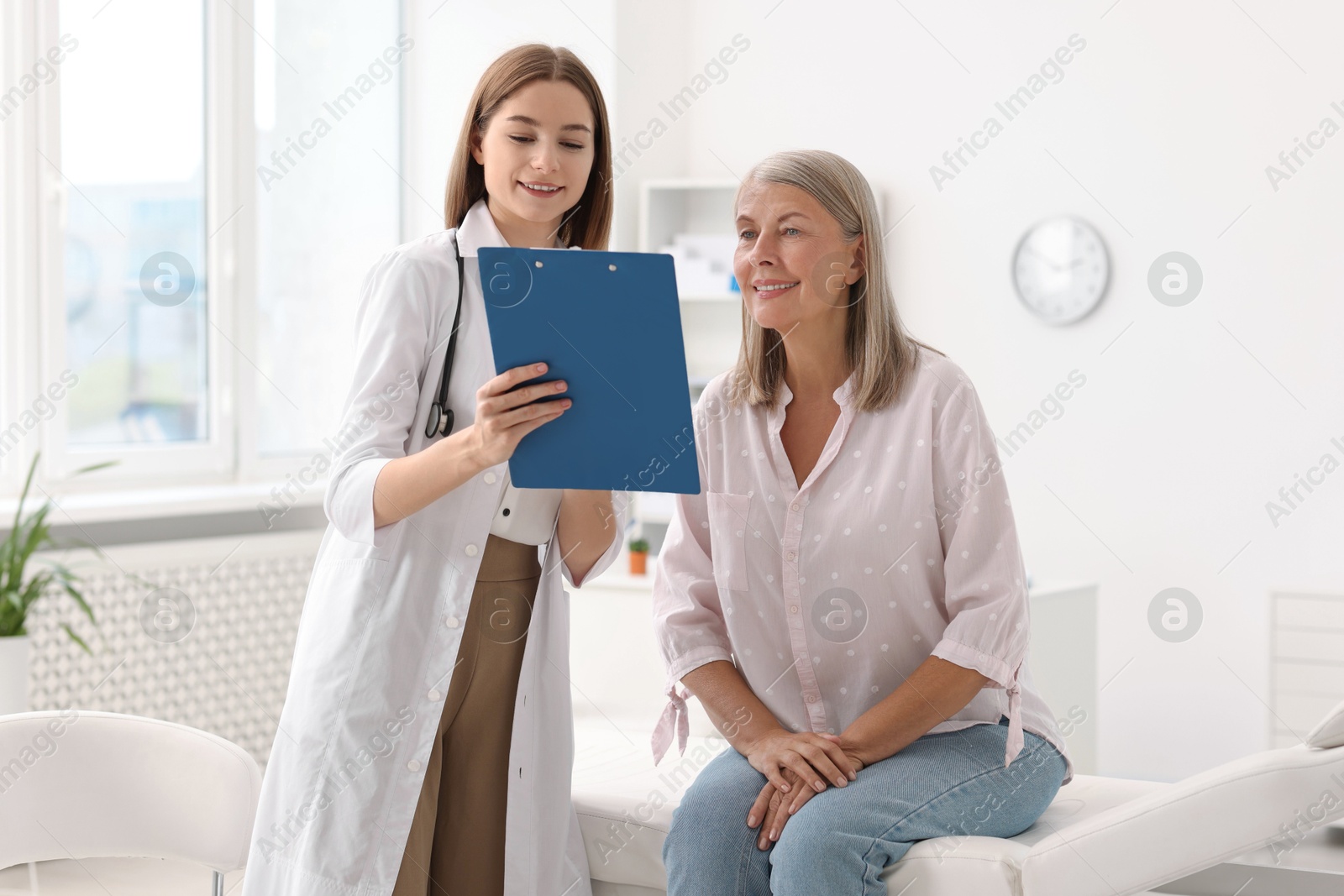 Photo of Smiling healthcare worker with clipboard consulting senior patient in hospital