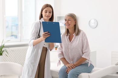 Smiling healthcare worker with clipboard consulting senior patient in hospital