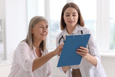 Photo of Smiling healthcare worker with clipboard consulting senior patient in hospital