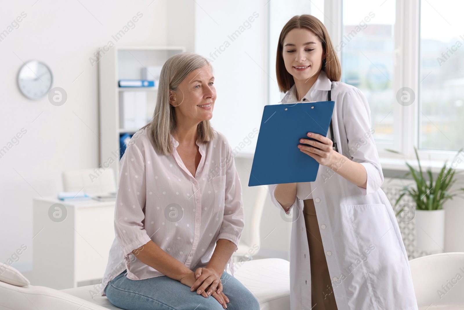 Photo of Smiling healthcare worker with clipboard consulting senior patient in hospital