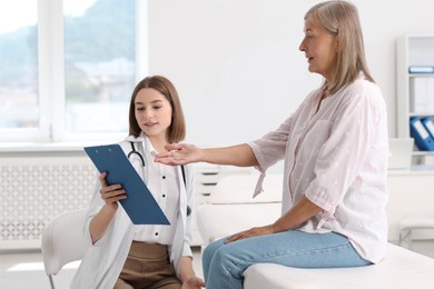 Photo of Smiling healthcare worker with clipboard consulting senior patient in hospital