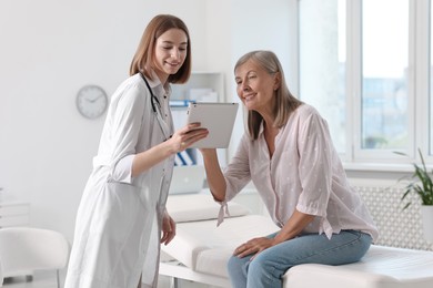 Smiling healthcare worker and senior patient checking analysis results on tablet in hospital