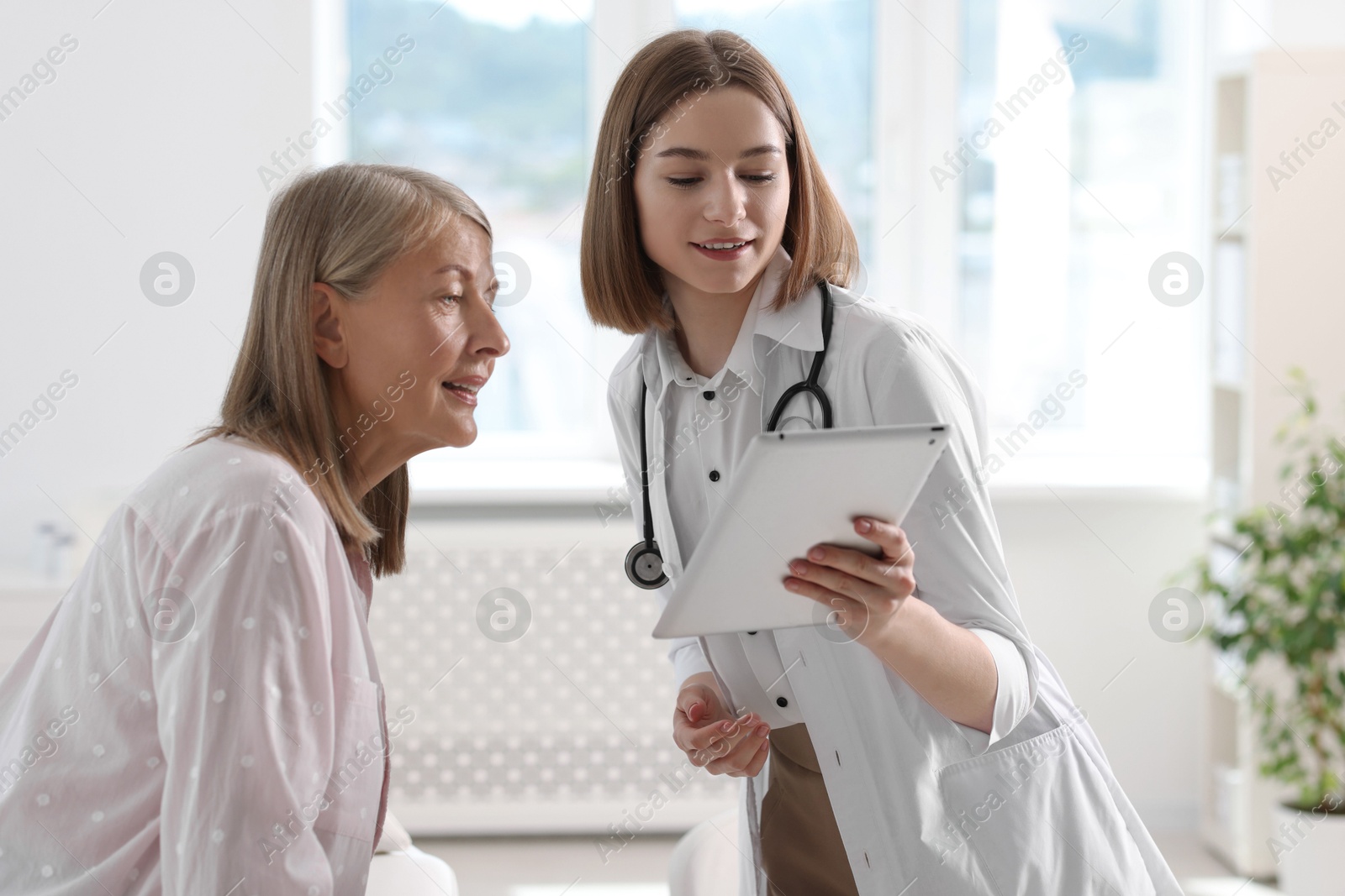 Photo of Smiling healthcare worker and senior patient checking analysis results on tablet in hospital