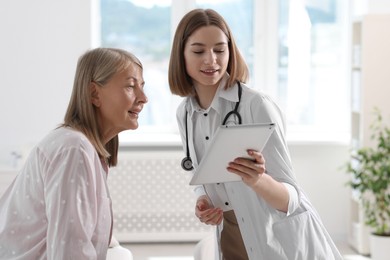 Smiling healthcare worker and senior patient checking analysis results on tablet in hospital