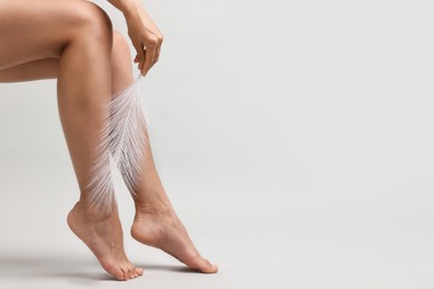 Photo of Woman with smooth legs and feather on grey background, closeup. Space for text