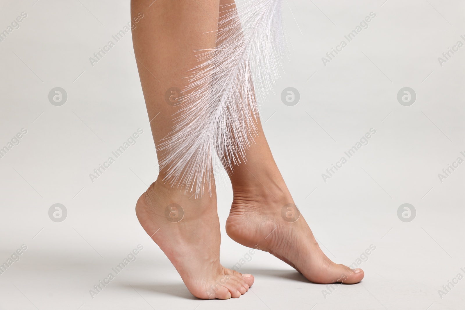 Photo of Woman with smooth legs and feather on grey background, closeup