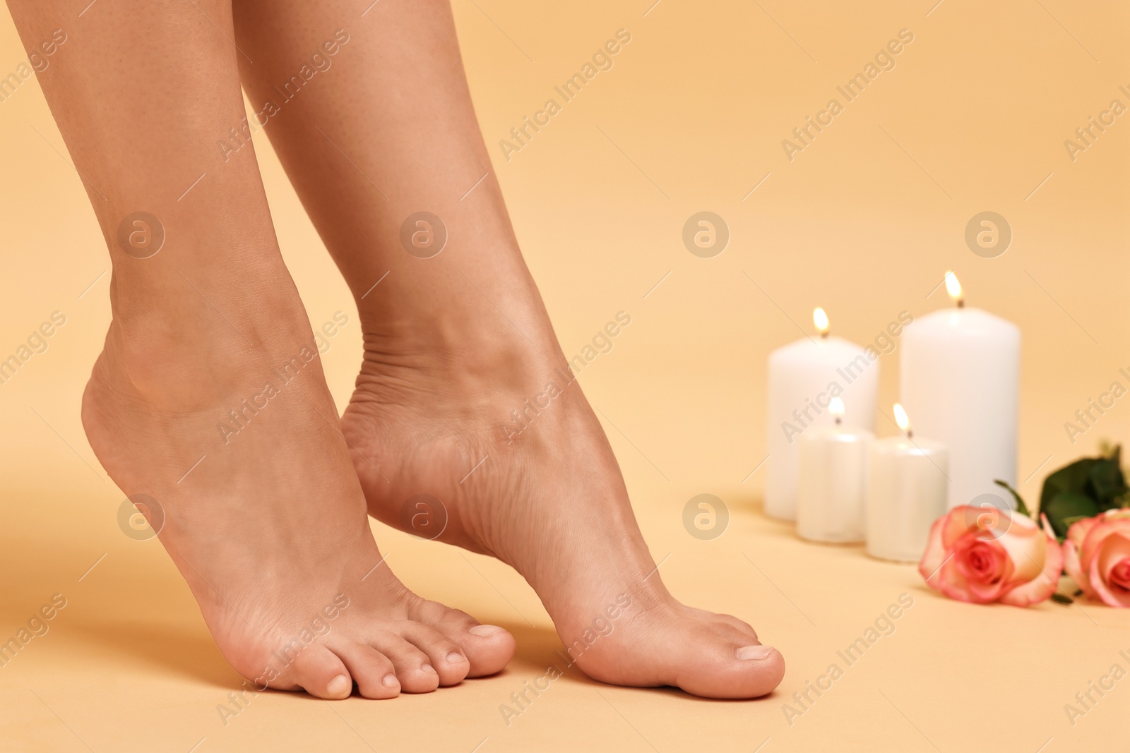 Photo of Woman with smooth feet, burning candles and roses on beige background, closeup