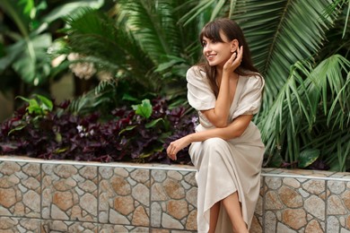 Smiling woman sitting near palm plants outdoors. Space for text