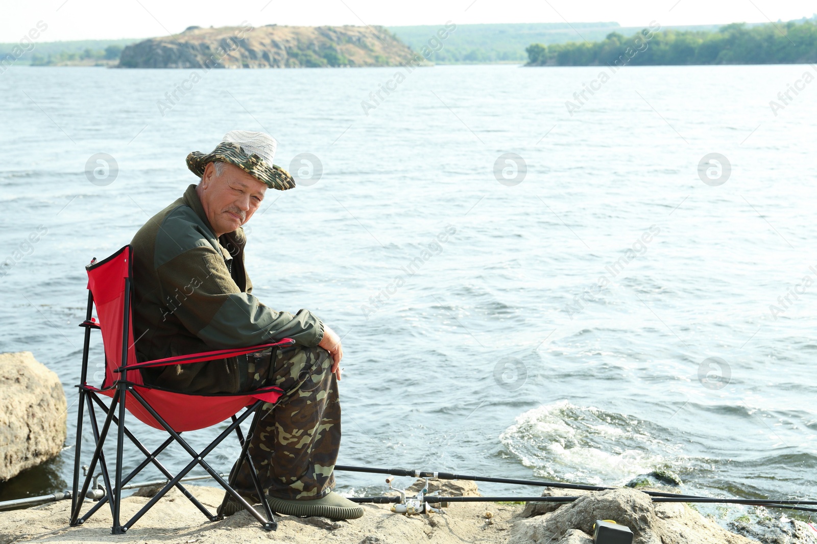 Photo of Fisherman with rod sitting on chair and fishing near lake at summer, space for text