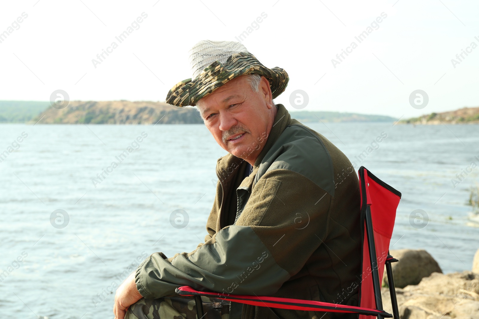 Photo of Fisherman with rod sitting on chair and fishing near lake at summer