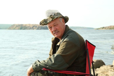 Fisherman with rod sitting on chair and fishing near lake at summer