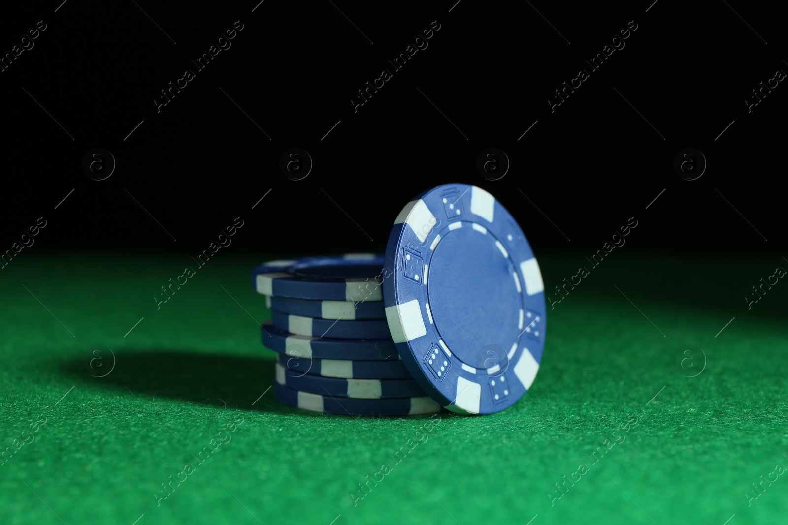 Photo of Poker chips on green table against dark background, closeup