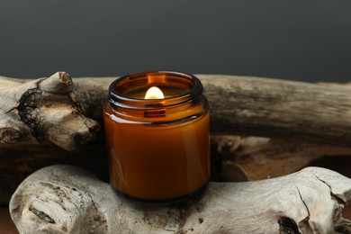 Beautiful burning candle on pieces of decorative wood against gray background, closeup