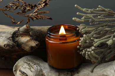 Beautiful burning candle, brunia plants and dry branch on pieces of decorative wood against gray background, closeup