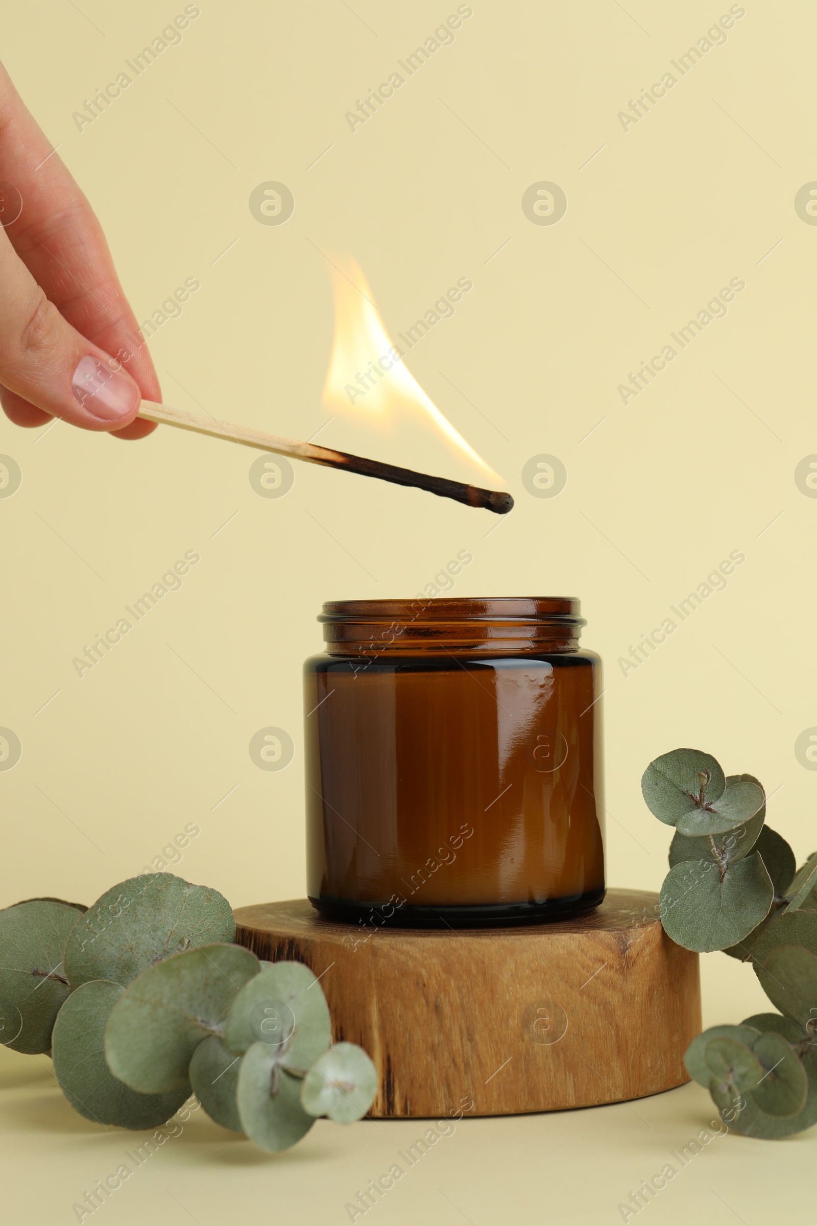 Photo of Woman lighting candle on pale yellow background, closeup