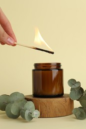 Photo of Woman lighting candle on pale yellow background, closeup