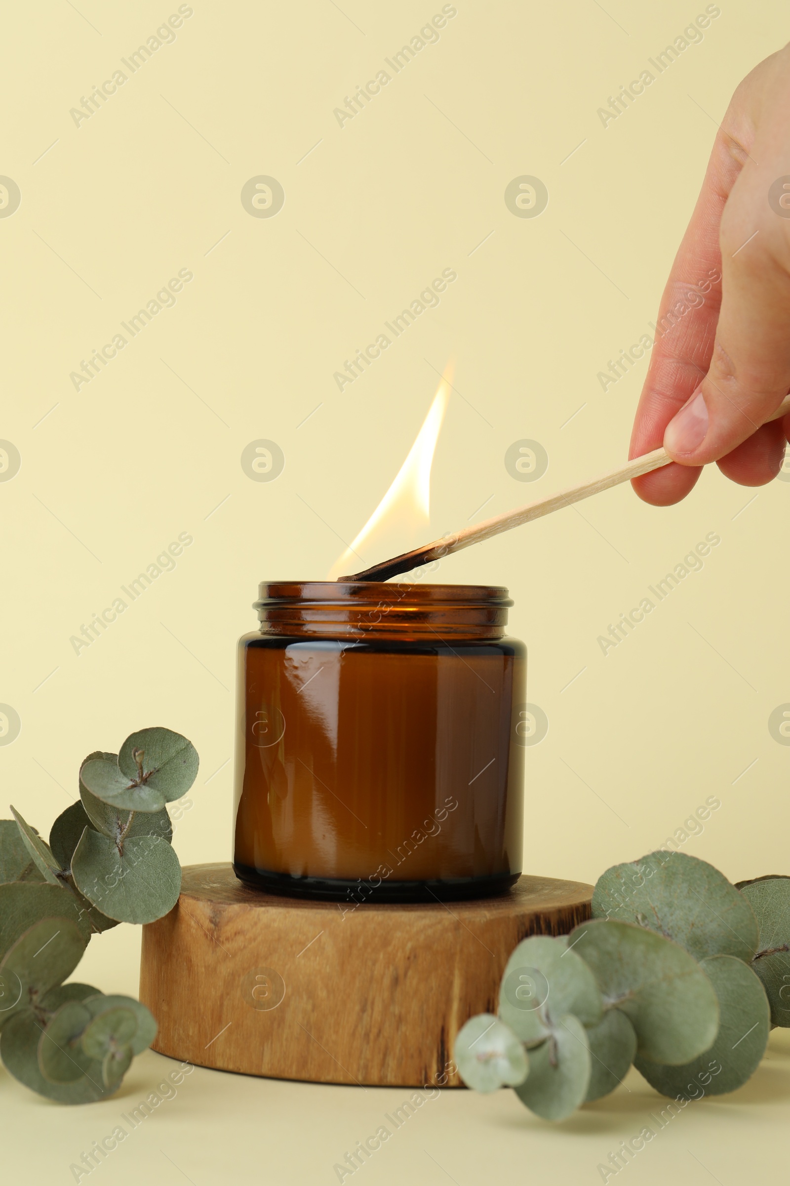 Photo of Woman lighting candle on pale yellow background, closeup