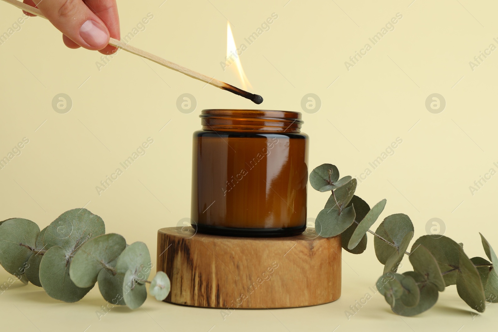 Photo of Woman lighting candle on pale yellow background, closeup