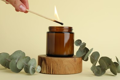 Woman lighting candle on pale yellow background, closeup