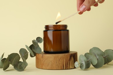 Photo of Woman lighting candle on pale yellow background, closeup