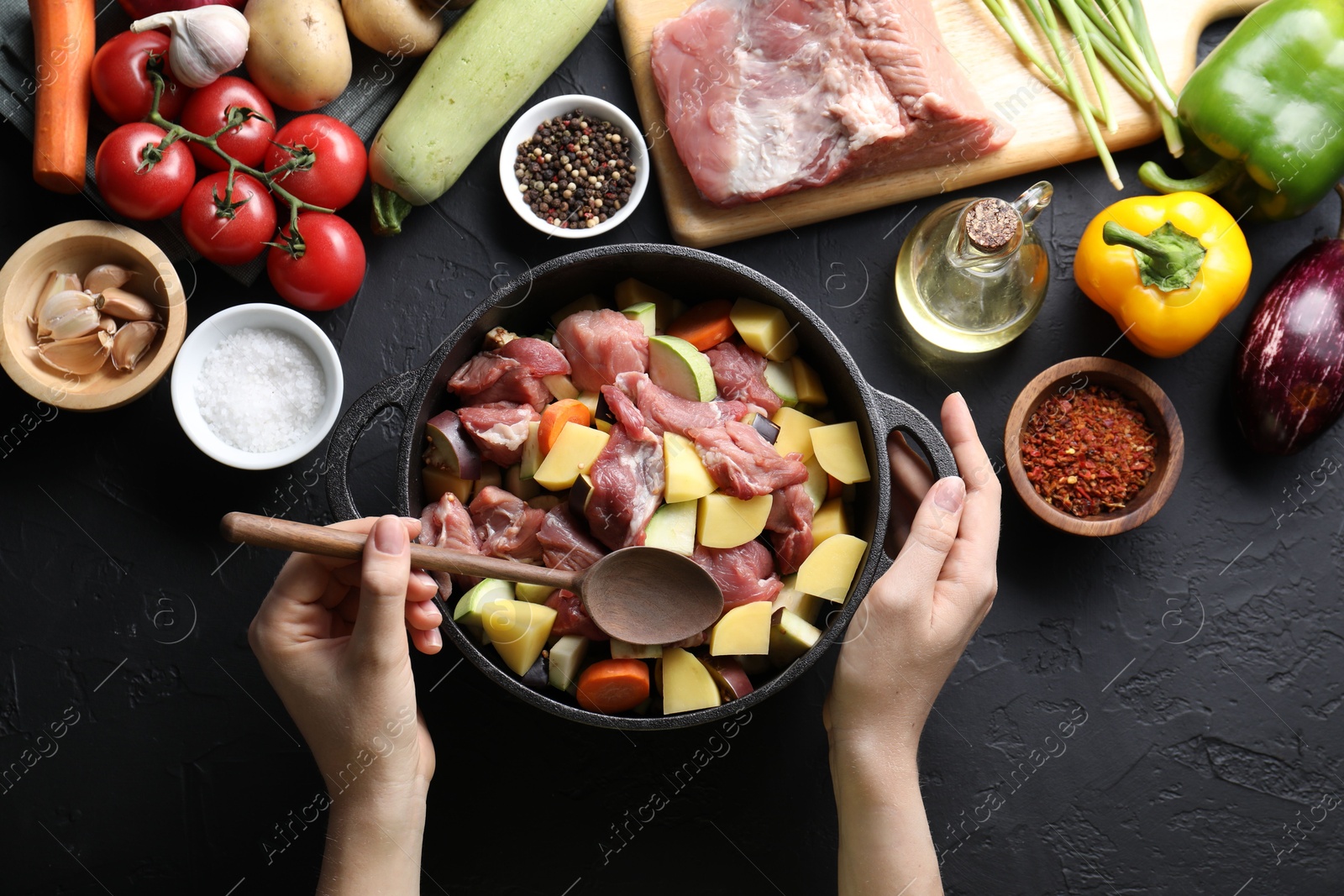 Photo of Cooking stew. Woman with uncooked meat, vegetables and pot on black table, top view