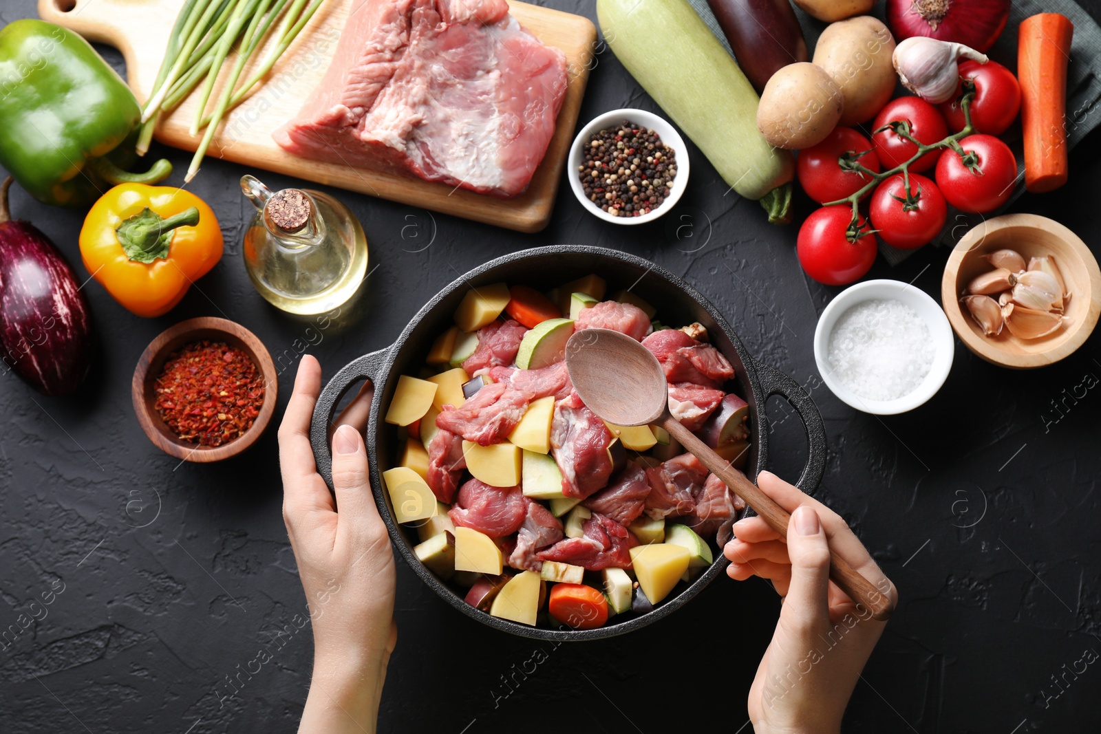 Photo of Cooking stew. Woman with uncooked meat, vegetables and pot on black table, top view