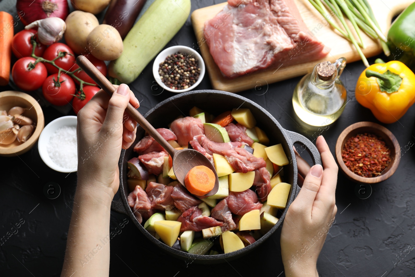 Photo of Cooking stew. Woman with uncooked meat, vegetables and pot on black table, top view