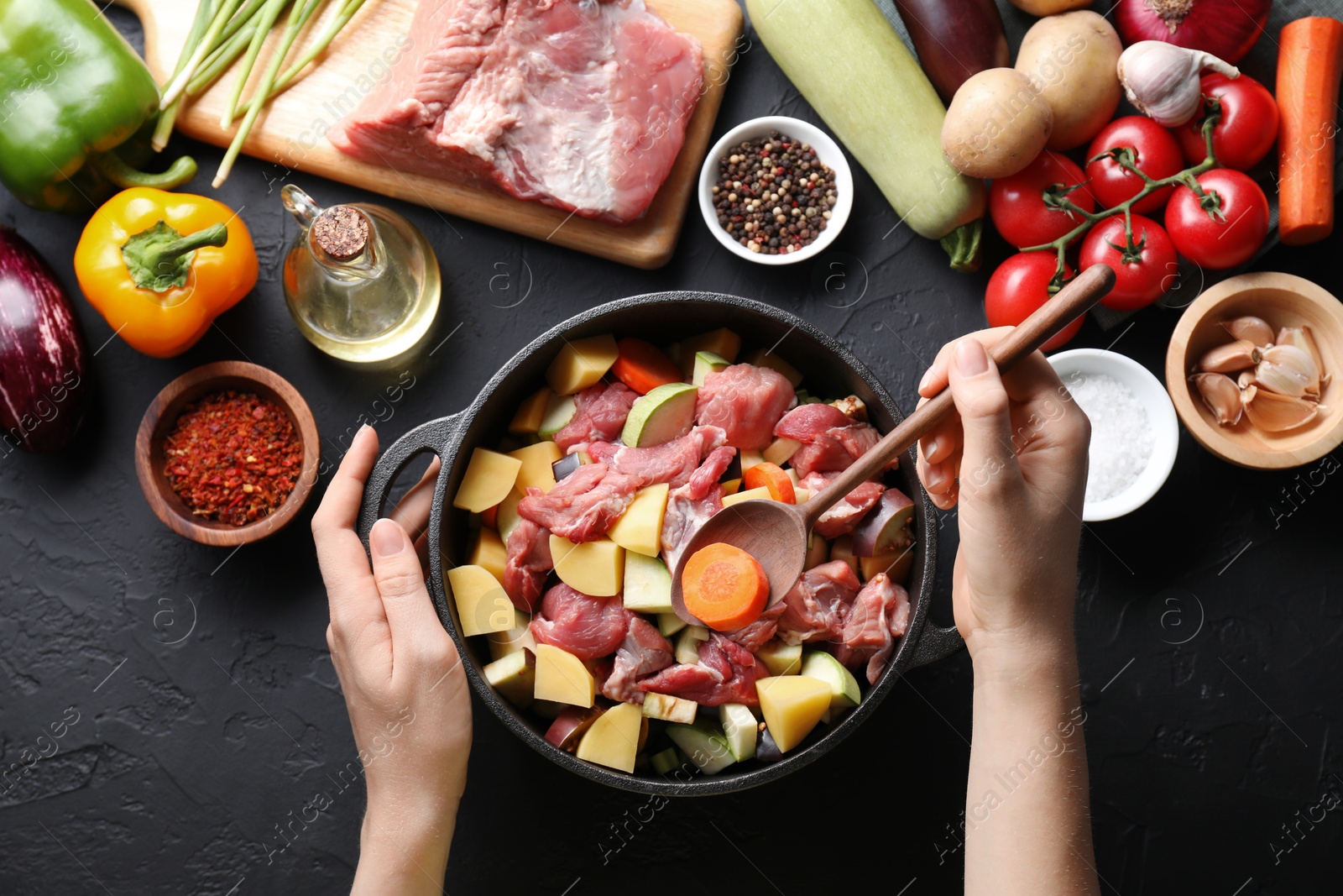 Photo of Cooking stew. Woman with uncooked meat, vegetables and pot on black table, top view