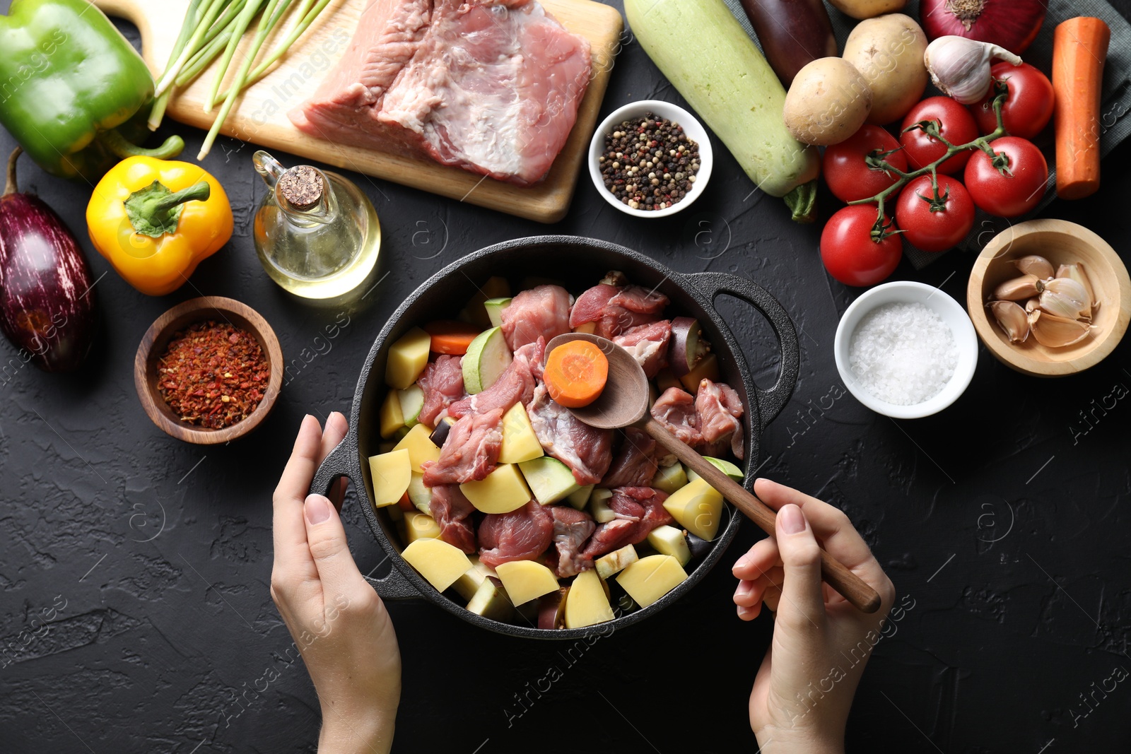 Photo of Cooking stew. Woman with uncooked meat, vegetables and pot on black table, top view