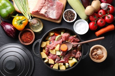 Photo of Cooking stew. Uncooked meat, vegetables and pot on black table, flat lay