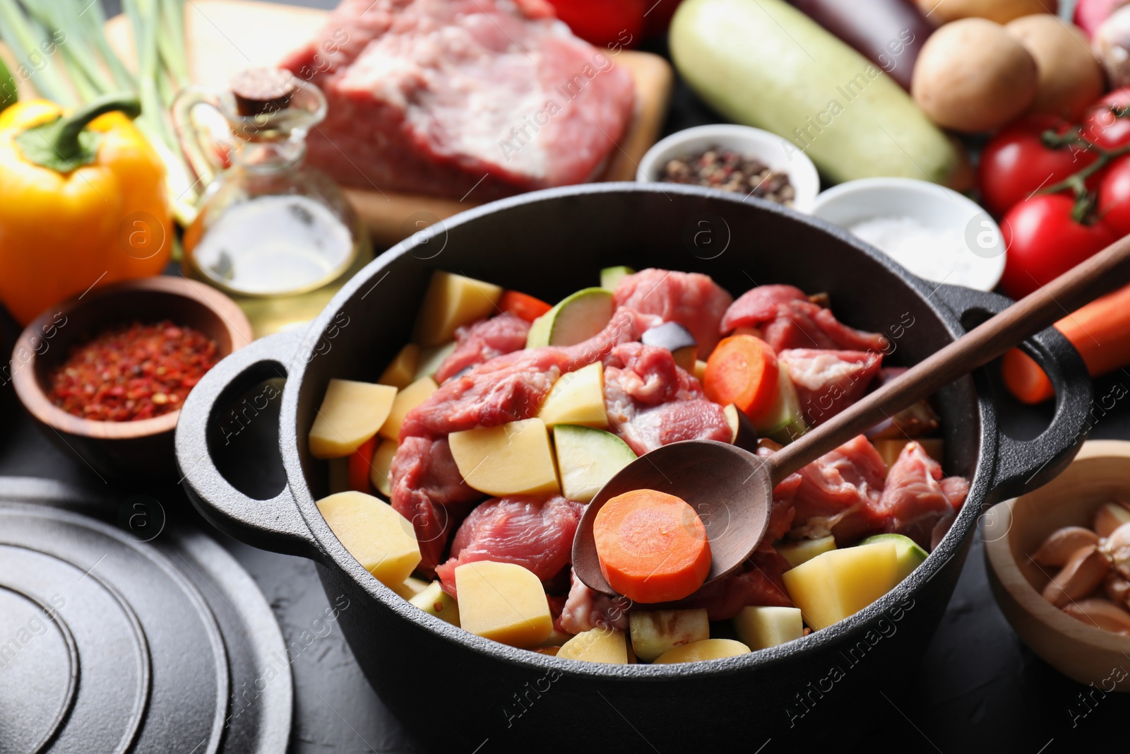 Photo of Cooking stew. Uncooked meat, vegetables and pot on black table