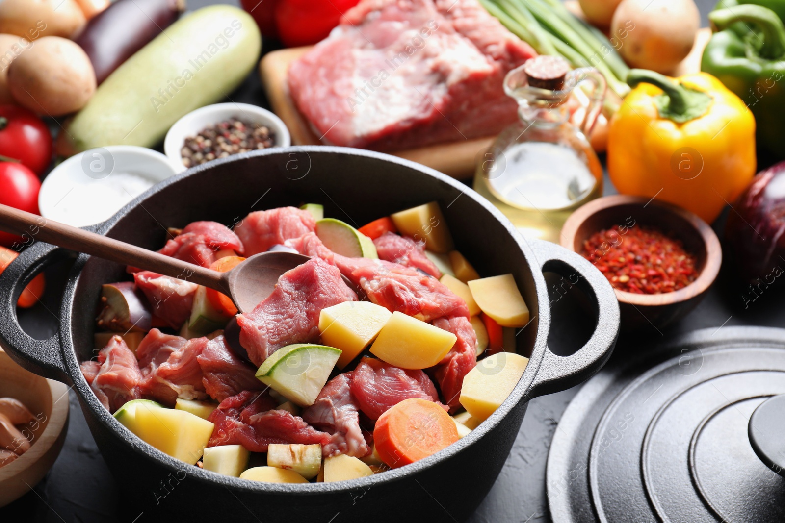 Photo of Cooking stew. Uncooked meat, vegetables and pot on black table