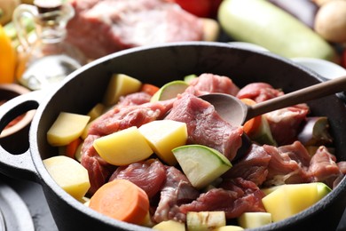 Photo of Cooking stew. Uncooked meat, vegetables and pot on black table, closeup