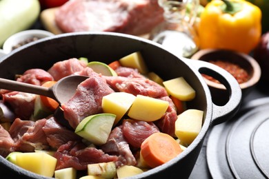 Photo of Cooking stew. Uncooked meat, vegetables and pot on black table, closeup