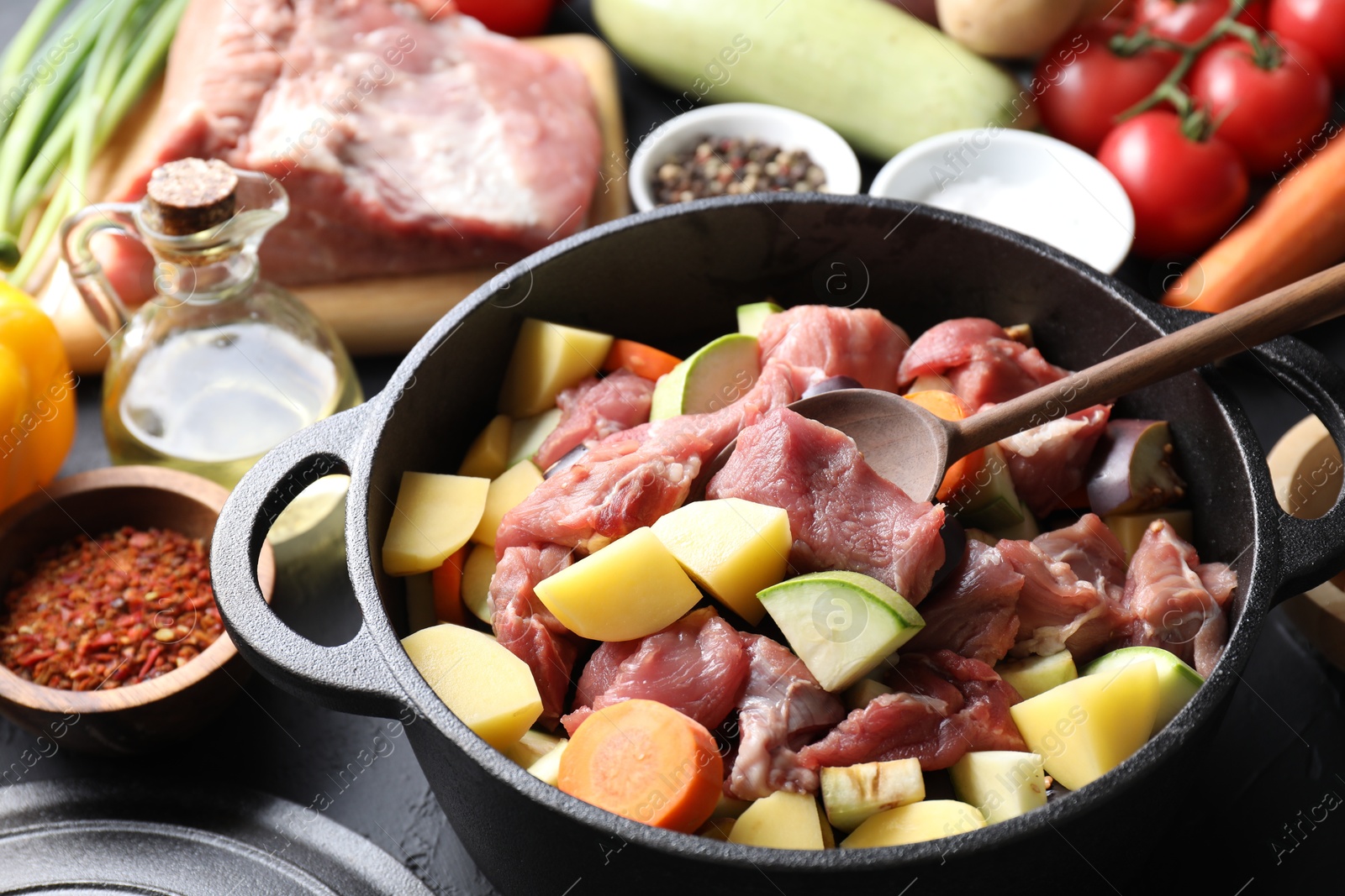 Photo of Cooking stew. Uncooked meat, vegetables and pot on black table, closeup