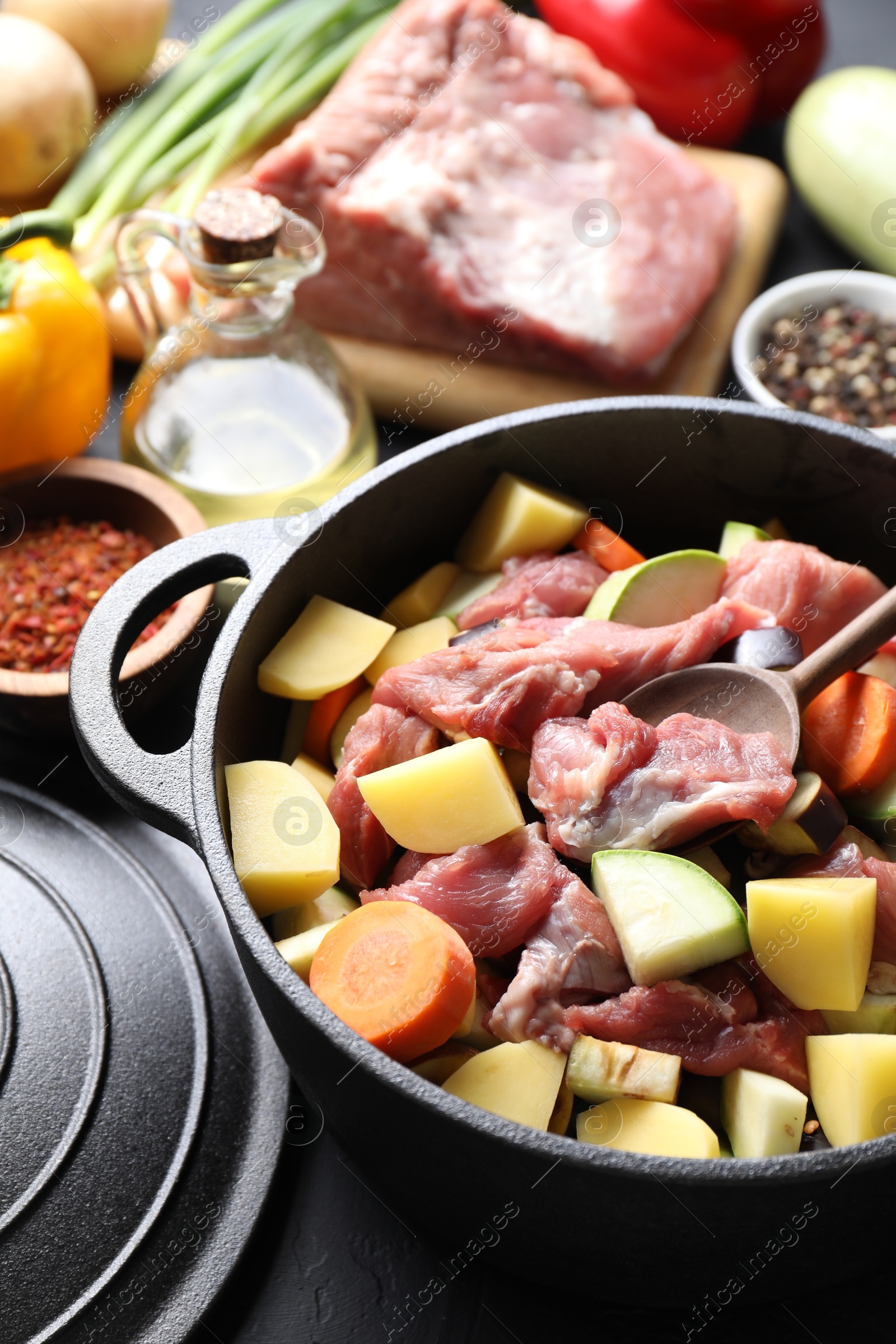 Photo of Cooking stew. Uncooked meat, vegetables and pot on black table, closeup