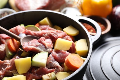 Photo of Cooking stew. Uncooked meat, vegetables and pot on black table, closeup