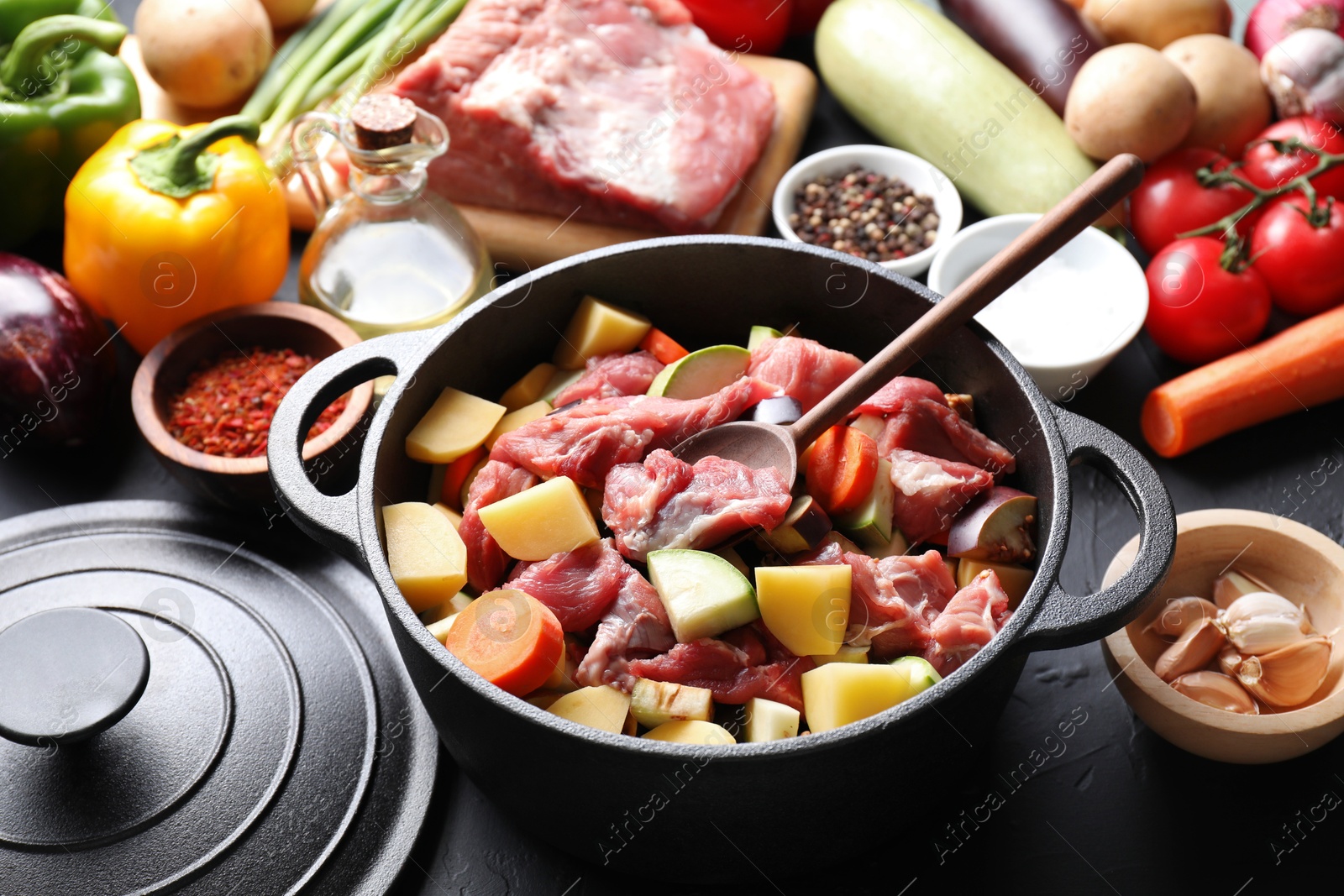 Photo of Cooking stew. Uncooked meat, vegetables and pot on black table