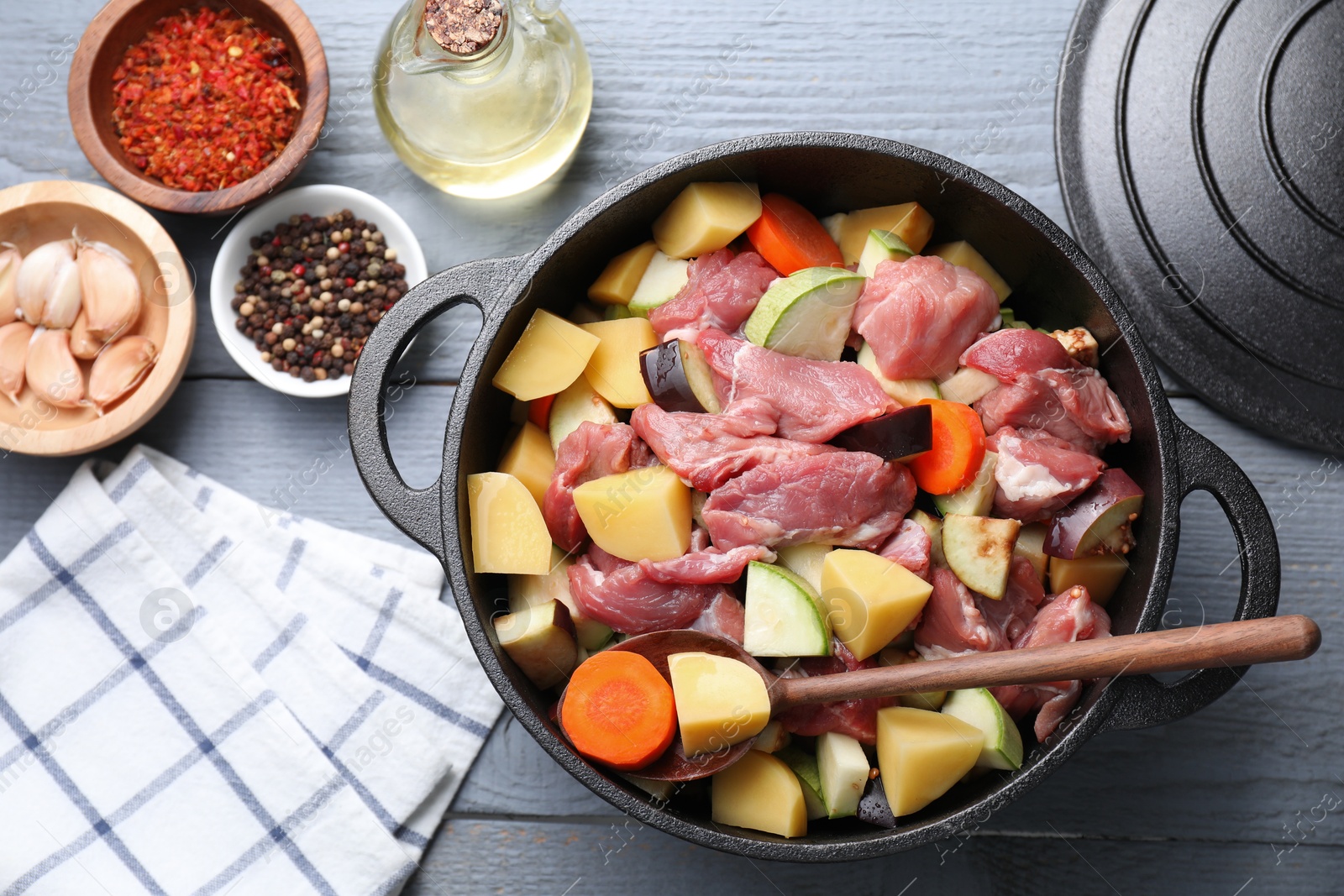 Photo of Uncooked meat and vegetables in pot on light grey wooden table, flat lay